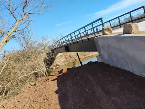 A poured concrete abutment in close foreground with fresh dark earth banked against it, the bridge it carries running away behind.