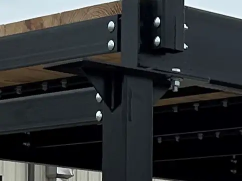 A close view of the bolted corner of a bridge kit, where the handrail post meets the deck beam through a bolted plate.
