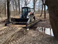 A skid steer loader driving across a steel bridge with timber decking.