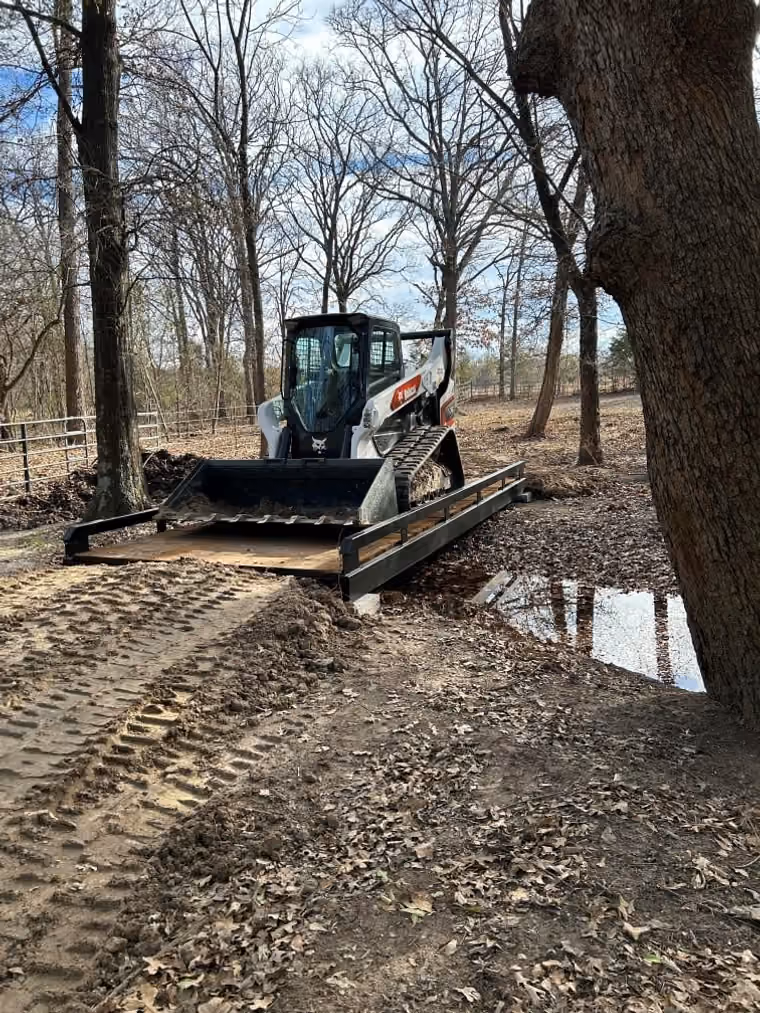 A skid steer loader driving across a steel bridge with timber decking.