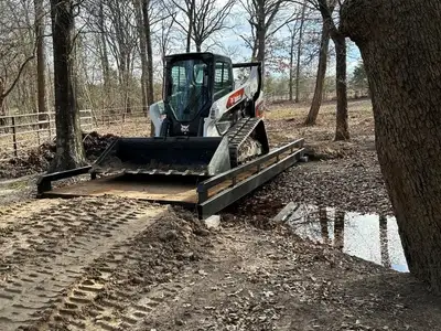 A skid steer loader driving across a steel bridge with timber decking.