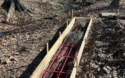 Timber formwork and pink rebar set in an excavated trench for a bridge abutment, in bare winter woodland.