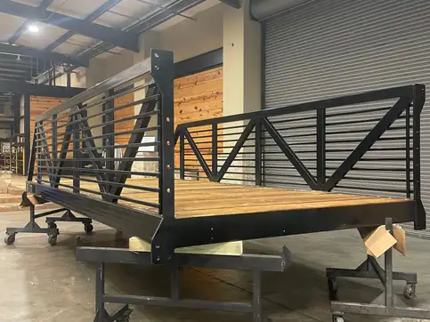 A decked bridge in a workshop fitted with a handrail of closely spaced horizontal steel bars, seen end on.