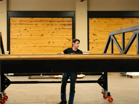 A man standing upright underneath a bridge span held on stands in a workshop, the deck passing well above his head.