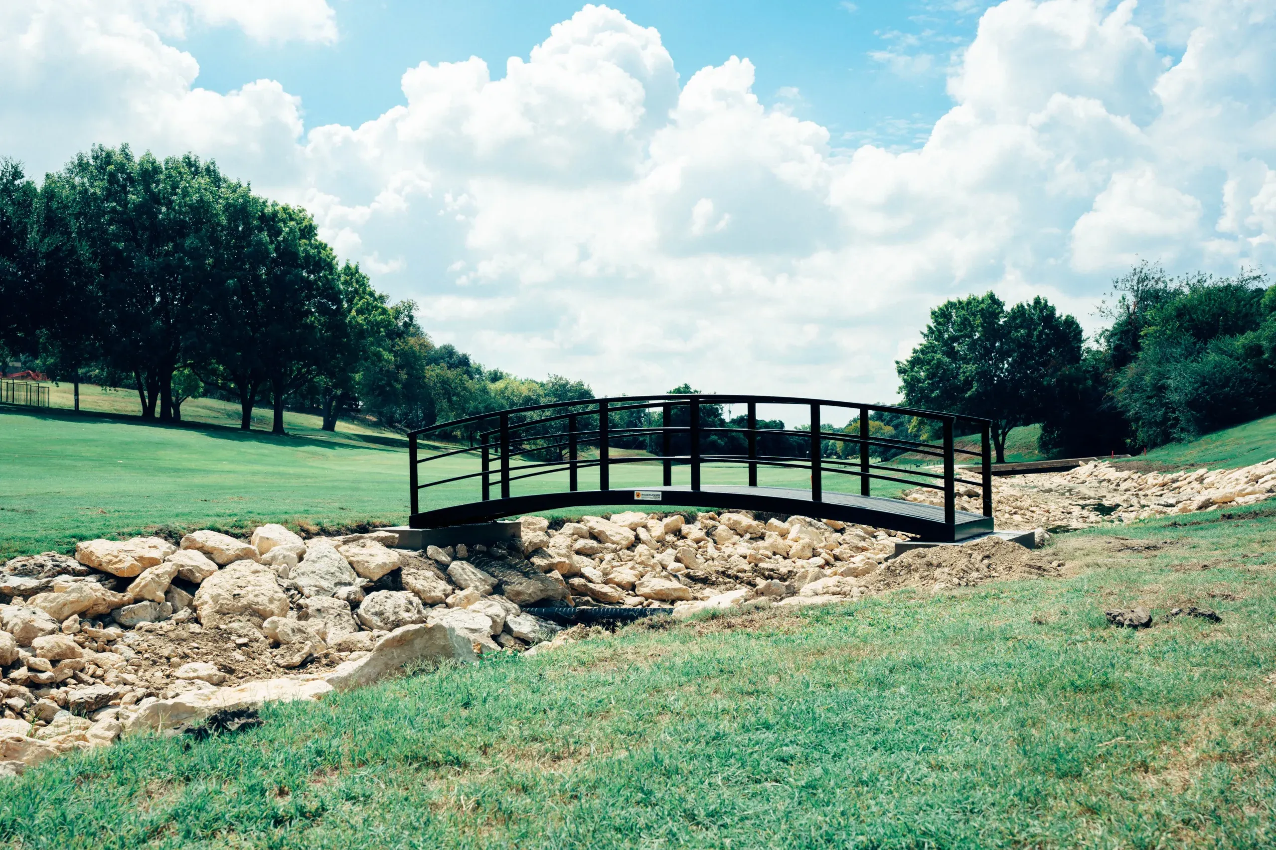 pedestrian bridge with arch design, black finish, over rocky creek