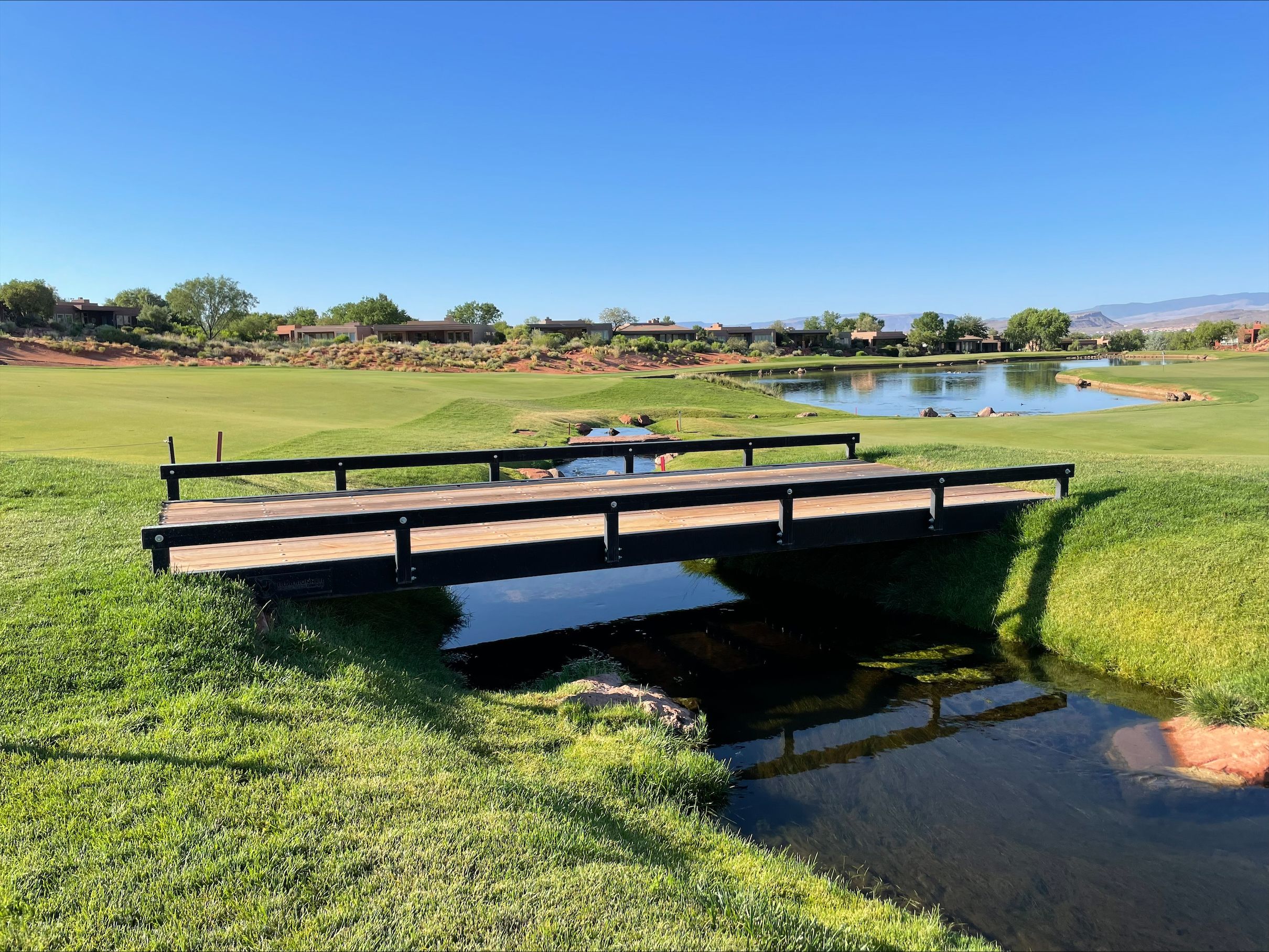 Installed modular bridge kit spanning a small creek on a golf course, featuring steel rails and wood decking integrated into the landscape.