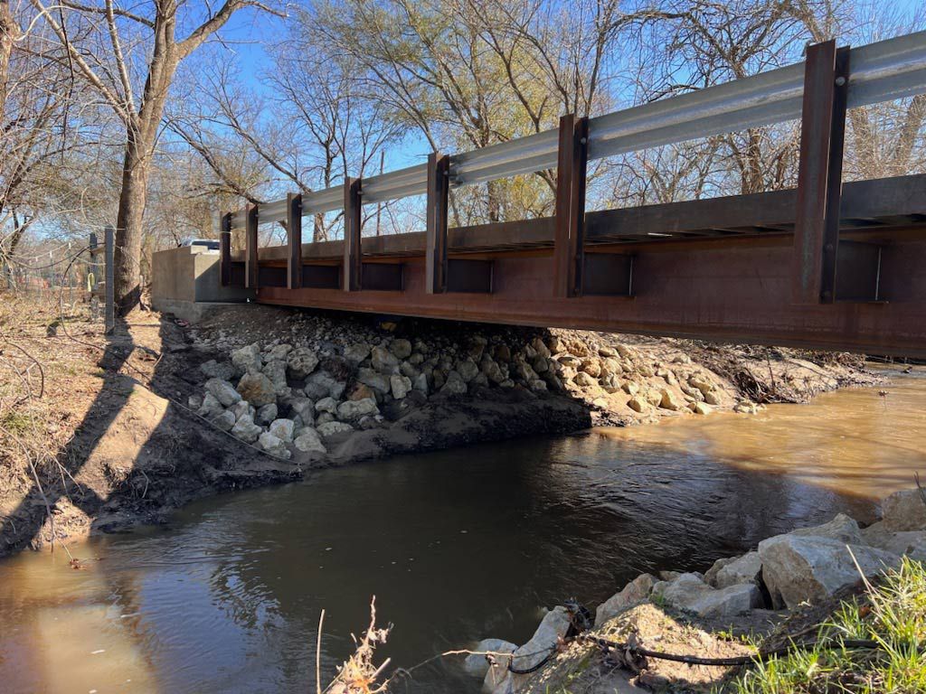 pedestrian bridge with weathered steel beams and guardrails over a creek