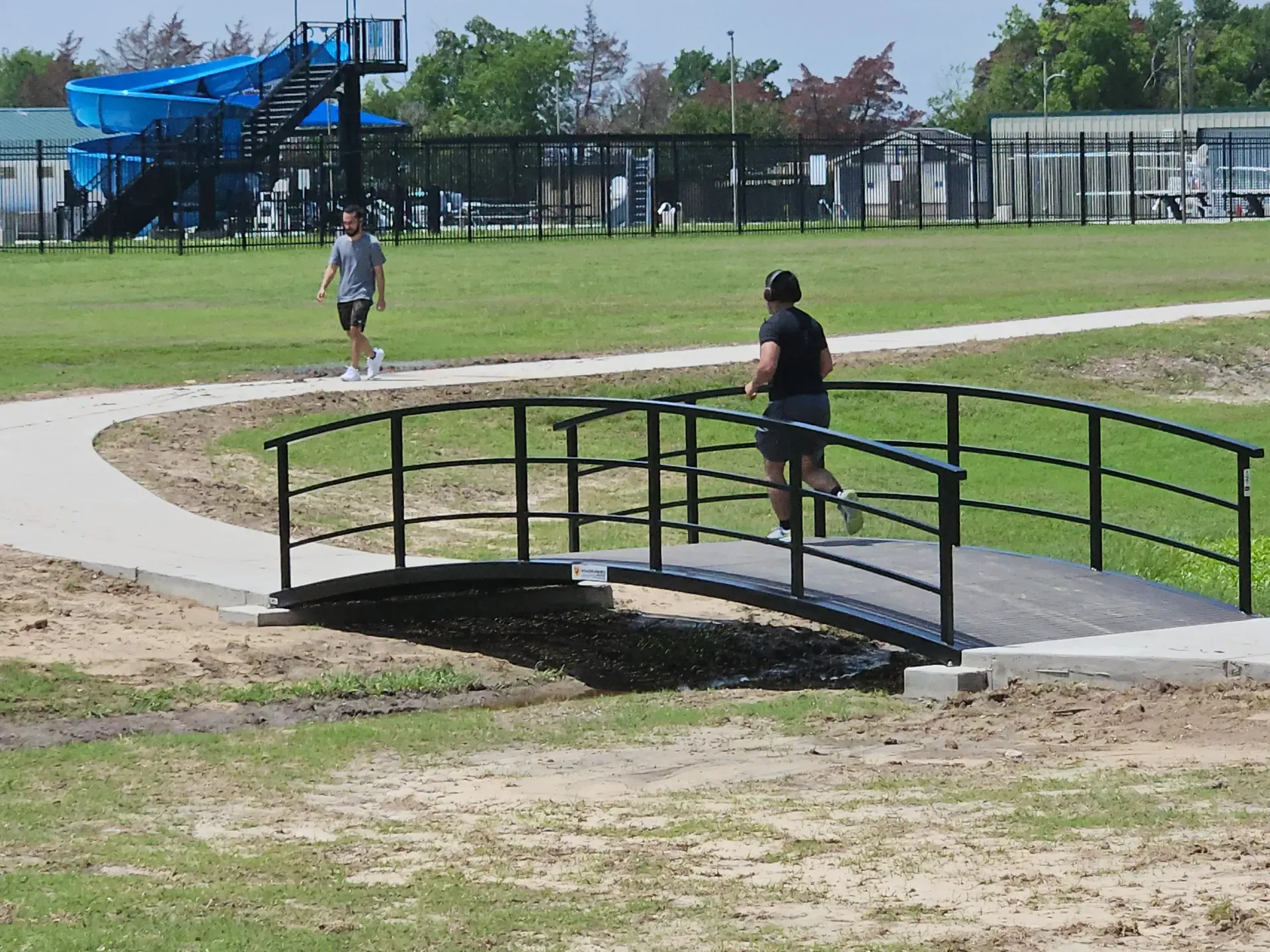 arch pedestrian bridge with black rails and wood deck over a creek