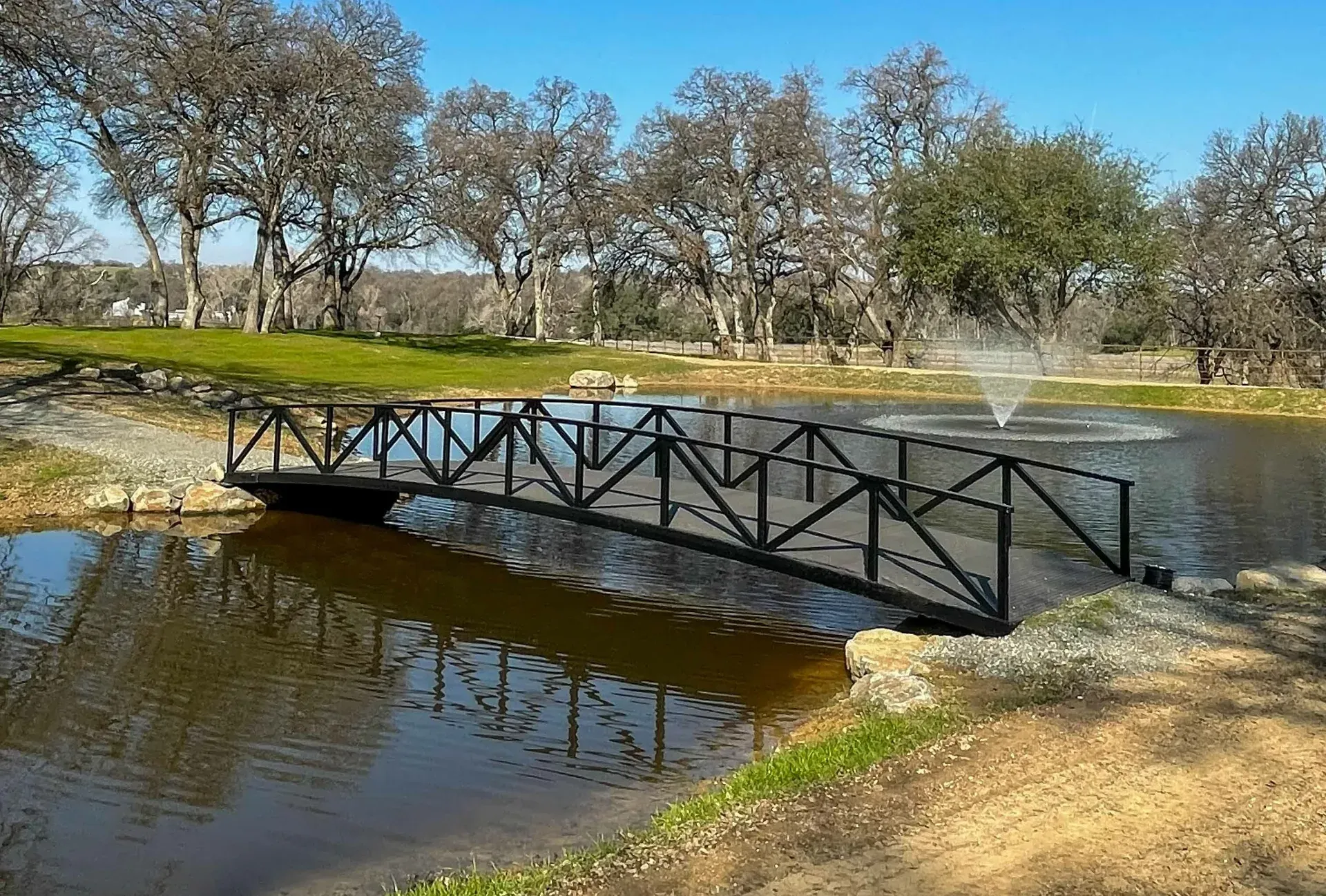 Pratt truss pedestrian bridge with painted finish over a pond.
