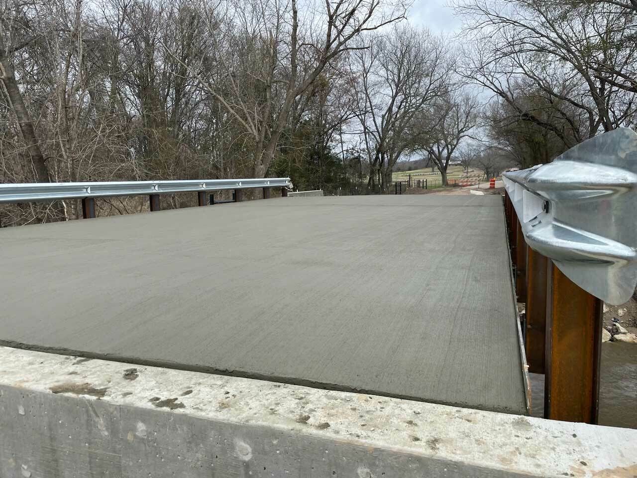 Concrete pedestrian bridge with guardrails, in final stage near a creek.