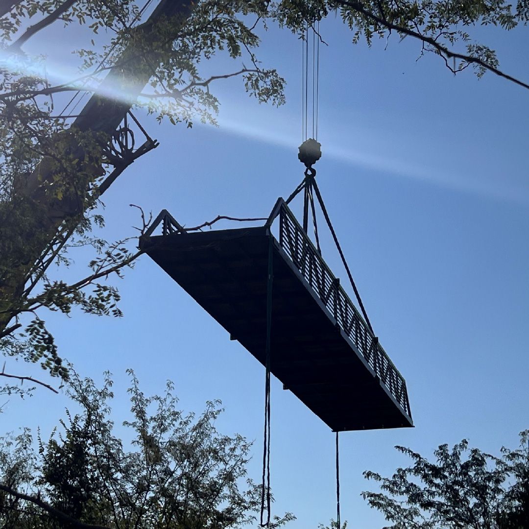 Crane lifting and installing a prefabricated Roadrunner Bridge steel bridge over a creek surrounded by trees.