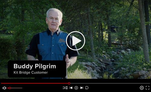Buddy Pilgrim stands in front of a wooded landscape and creek as he gives a testimonial about his Roadrunner Bridge.