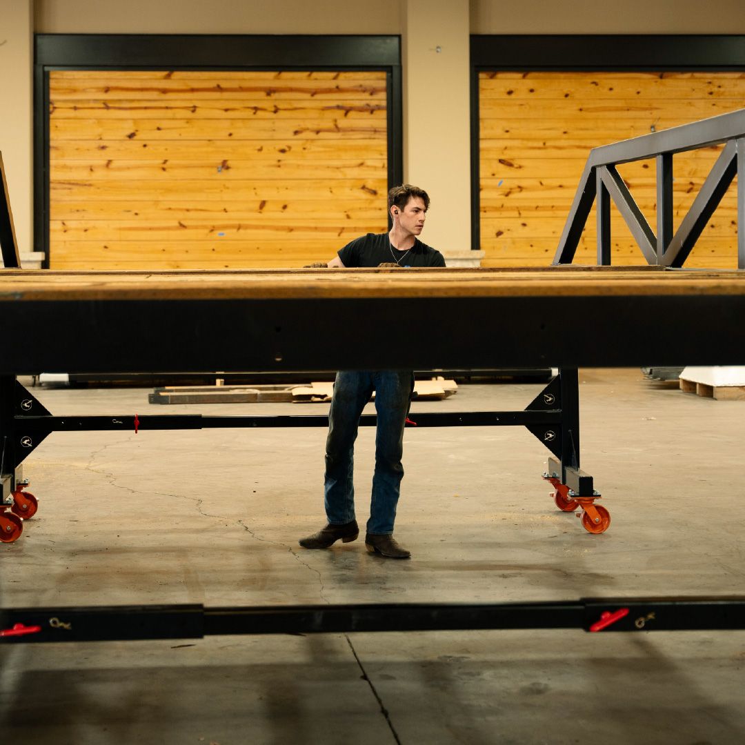 Worker assembling a steel Roadrunner Bridge frame inside a fabrication shop before installation.