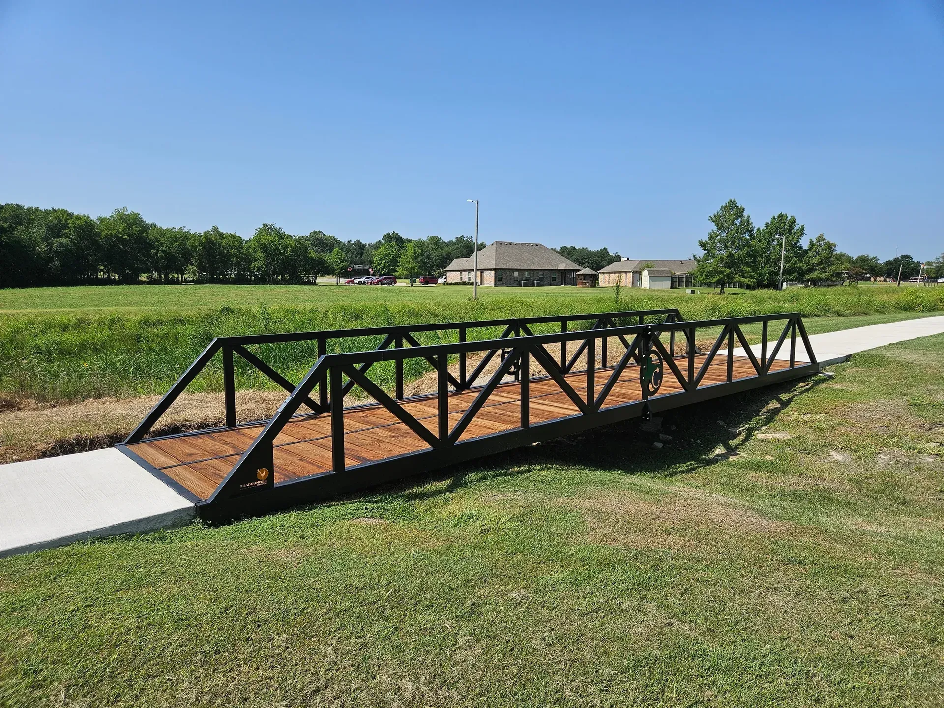 Warren truss pedestrian bridge with painted finish and timber deck in grassy area.