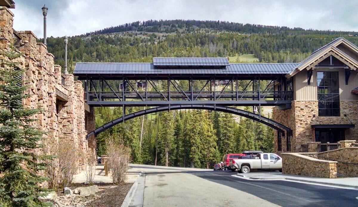 Pedestrian bridge with arched steel truss design and solar panels, set in a scenic area.