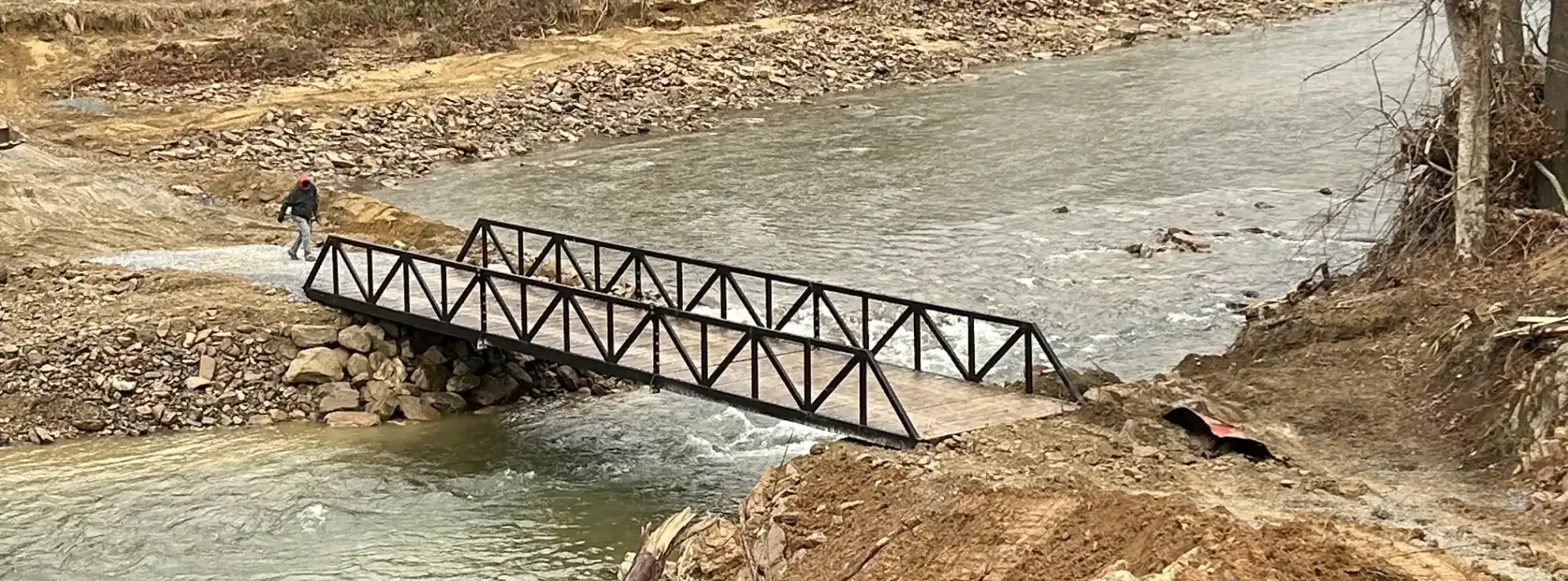 Warren truss pedestrian bridge with painted finish over creek.
