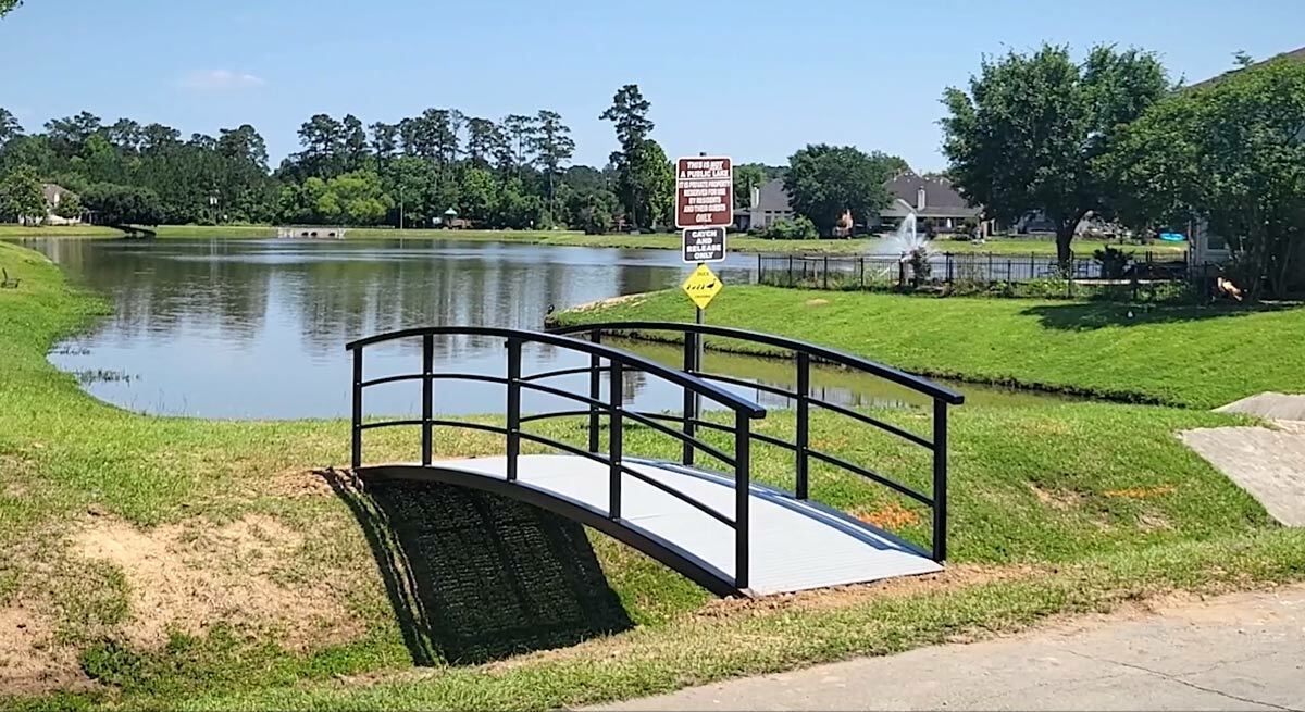 Pedestrian bridge with arched steel frame and black finish over a creek.