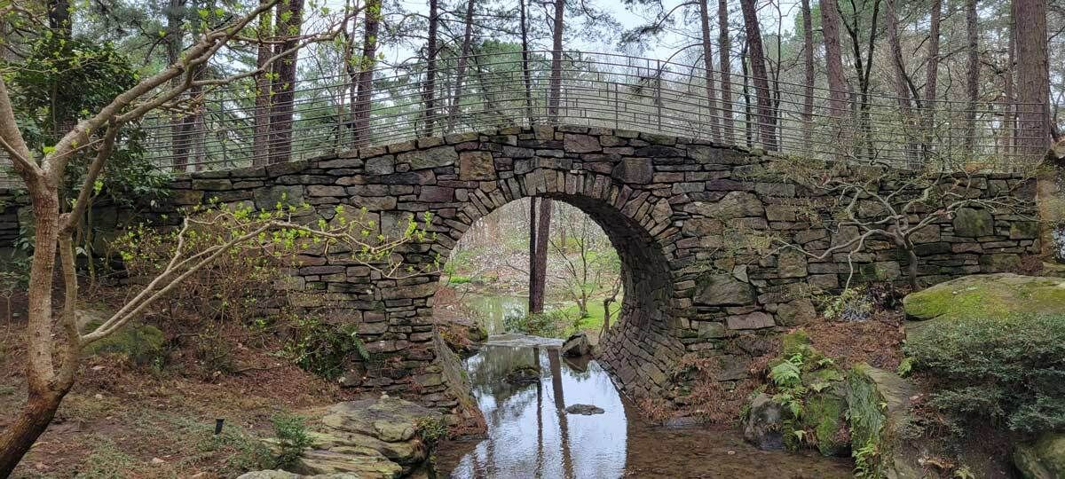 stone arch bridge with a curved design over a creek in a forested area