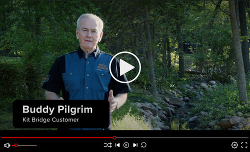 Buddy Pilgrim stands in front of a wooded landscape and creek as he gives a testimonial about his Roadrunner Bridge.